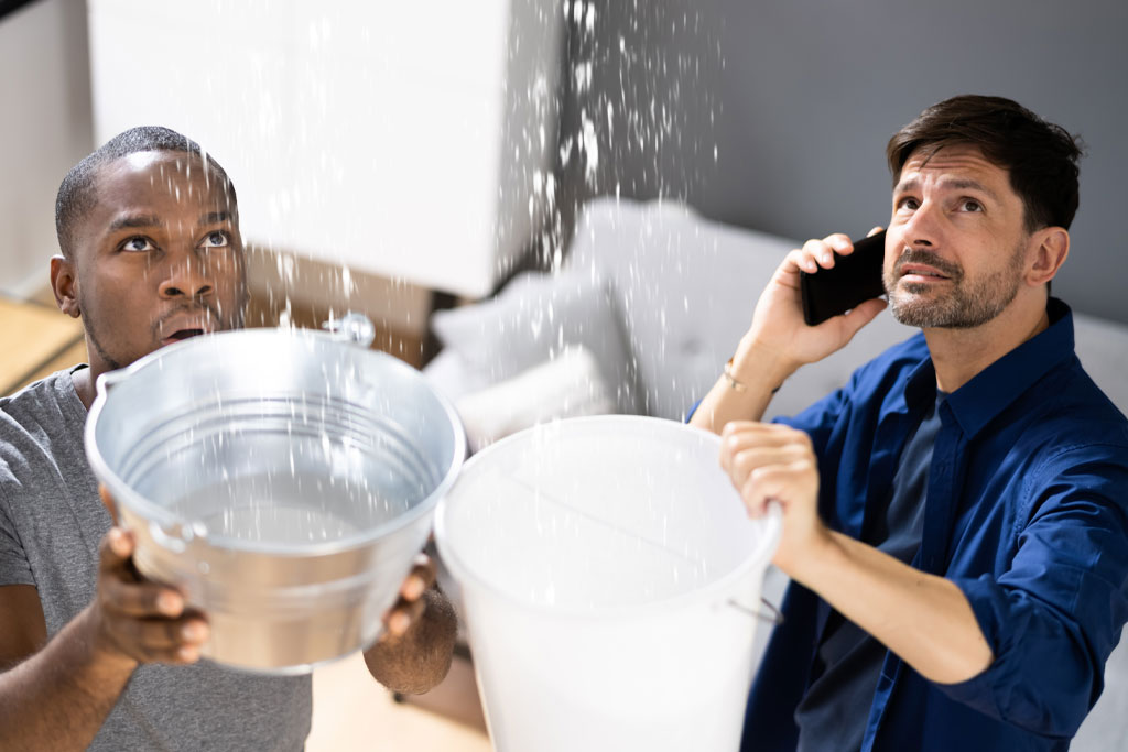 Two men holding buckets to contain water from a pipe burst